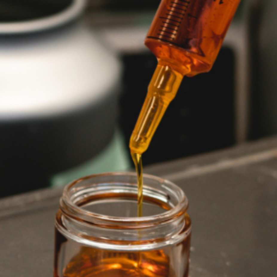 Golden delta 8 distillate being syringed into a glass jar for bulk sale, showcasing the viscous quality of the concentrate.